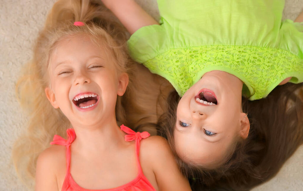 Gelukkige kleine meisjes blond en brunette liggen op hun rug en lachen. Bovenaanzicht. - Foto, afbeelding
