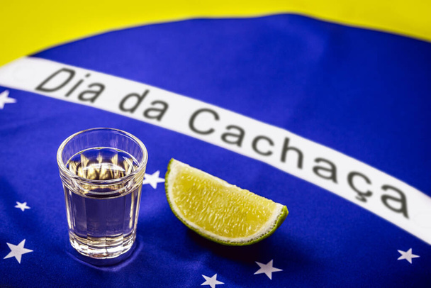 cup of cachaa or Brazilian pinga, with the Brazilian flag in the background in celebration of the national day of cachaca - Photo, Image