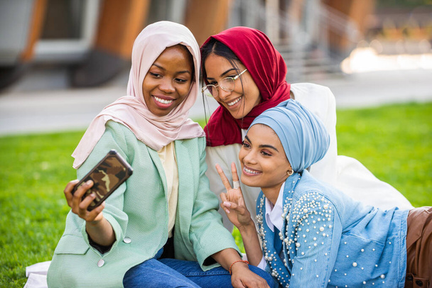 Multiethnic group of muslim girls wearing casual clothes and traditional hijab bonding and having fun outdoors - 3 arabic young girls - Foto, imagen