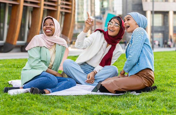 Multiethnic group of muslim girls wearing casual clothes and traditional hijab bonding and having fun outdoors - 3 arabic young girls - Фото, изображение