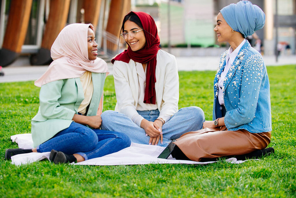 Multiethnic group of muslim girls wearing casual clothes and traditional hijab bonding and having fun outdoors - 3 arabic young girls - Photo, Image