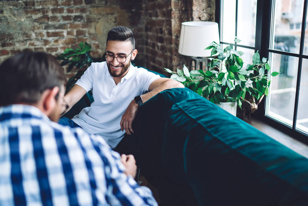 High angle of happy bearded male colleagues in casual outfits and glasses smiling and talking about business project in office - Fotoğraf, Görsel