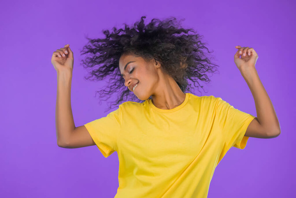 Happy curly haired african woman dancing, having fun, rejoices on purple studio background. Champion girl. Concept of celebrating, party, winning - Zdjęcie, obraz