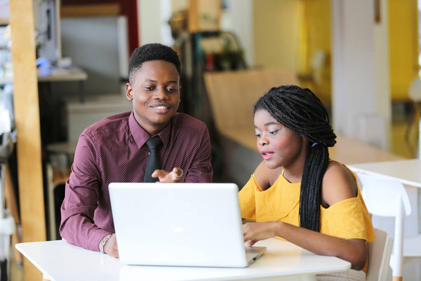若いアフリカ系アメリカ人の男性と女の子がオフィスのノートパソコンで働いている姿. - 写真・画像