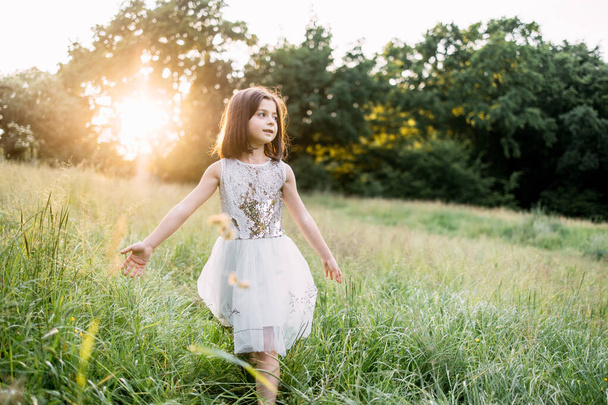 Playful child in summer dress walking among high grass - Foto, afbeelding