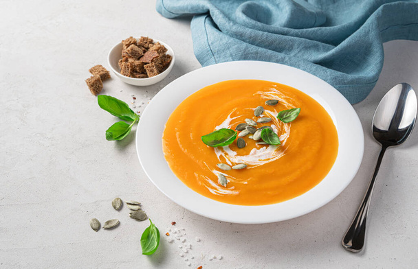 Autumn pumpkin cream soup with basil and cream on a gray background. Side view, space for copying. - 写真・画像
