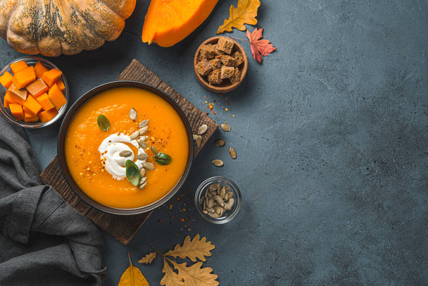 Pumpkin cream soup in a black bowl on an autumn background. Top view, copy space. - Фото, изображение
