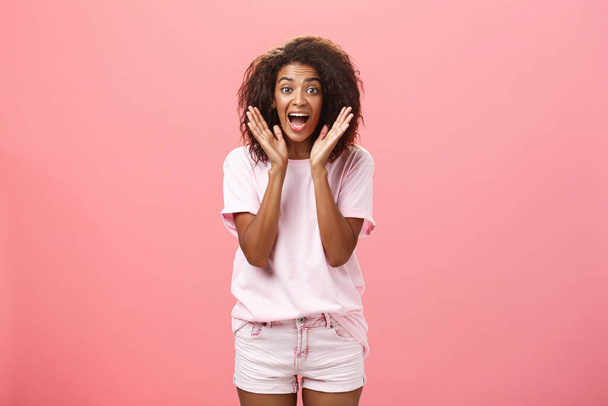 Indoor shot of expressive excited attractive dark-skinned adult woman in casual outfit yelling from amazement and joy holding palms near face reacting on awesome news with excitement and happiness - Foto, Bild