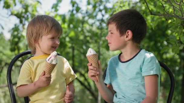 infancia sin preocupaciones, hermanos lindos se divierten comiendo helado fresco en el día caliente y frotarse la nariz con postre dulce durante las vacaciones de verano - Metraje, vídeo