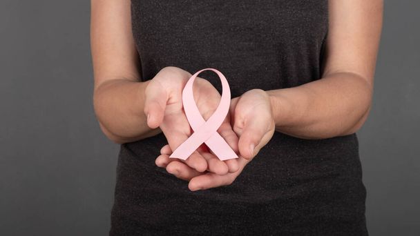 girl holding a pink ribbon in her palms a symbol of the fight against breast cancer. - Foto, imagen