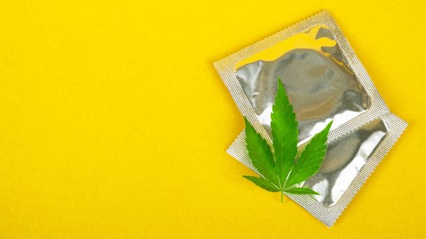 préservatif et feuille de cannabis avec espace de copie sur fond jaune, maquette de drogues sexuelles. - Photo, image