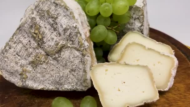  A plate of assorted mouldy goat's milk cheeses on a wooden Board with green grapes - Footage, Video