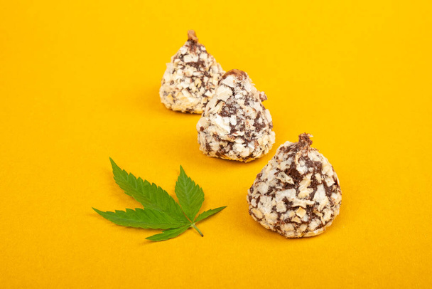 chocolate candies with nuts and marijuana on yellow background. food with recreational cannabis. - Foto, imagen
