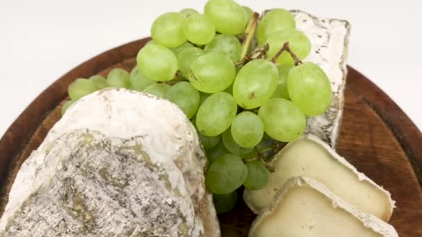  Тарелка разнообразных заплесневелых козьих сыров на деревянной доске с зеленым виноградом - Кадры, видео