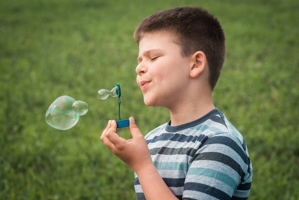 A portrait of a happy, sweet boy blowing bubbles. Kid blows bubbles funny. The child smiles in spring or summer. Happy childhood - Photo, Image