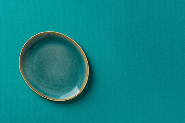 Oval turquoise blue ceramic plate with brown border over textured teal background. Modern empty dishes and tableware of noble trendy color for stylish food design. Copy space. Top view.  - Photo, Image