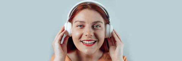 cheerful happy smiling young woman in white headphones listening to music on a grey background - Photo, image