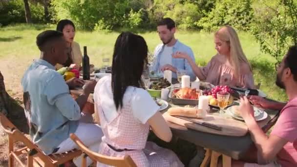 Toma de mano de hombres y mujeres jóvenes que pasan un maravilloso día de verano almorzando juntos al aire libre en el hermoso parque - Imágenes, Vídeo