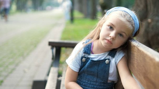 Petite enfant sérieuse assise seule sur un banc dans un parc d'été. - Photo, image