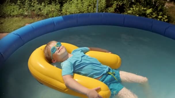 Funny baby boy sunbathing on safety buoy at inflatable rubber swimming pool relaxing - Footage, Video