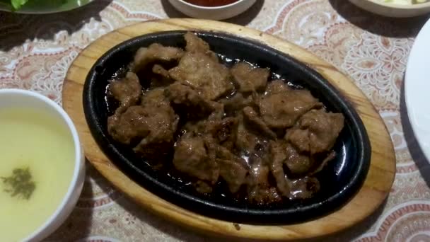 Top view of a table covered with Korean dishes. Sizzle pieces of meat, vegetable salads, a bowl of rice in a hot frying pan - Footage, Video