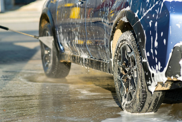 Κοντινό πλάνο του αρσενικού οδηγού πλύσιμο του αυτοκινήτου του με ανέπαφη υψηλής πίεσης αεριωθούμενο νερό στο πλυντήριο αυτοκινήτων self service. - Φωτογραφία, εικόνα