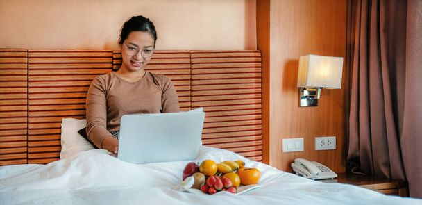 Immagine di turisti usato laptop e mangiare frutta sul letto nella camera d'albergo di lusso, concetto di cibo sano. - Foto, immagini