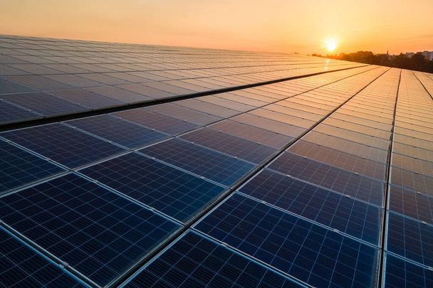 Mavi fotovoltaik güneş panelleri gün batımında temiz ekolojik elektrik üretmek için çatıya monte edildi. Yenilenebilir enerji konsepti üretimi. - Fotoğraf, Görsel