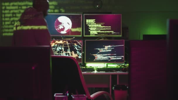 Moderno hacker criminale che si siede di fronte a monitor di computer con codici sugli schermi, mettendo sul cofano e iniziando a lavorare nella stanza buia dell'ufficio - Filmati, video