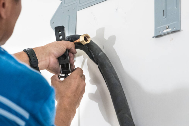Technician installing indoor air conditioner compressor condenser copper pipe on wall - Photo, Image