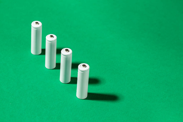 White AA batteries on a green background. Space for text. Recycling of rechargeable NiMH batteries. - Photo, image