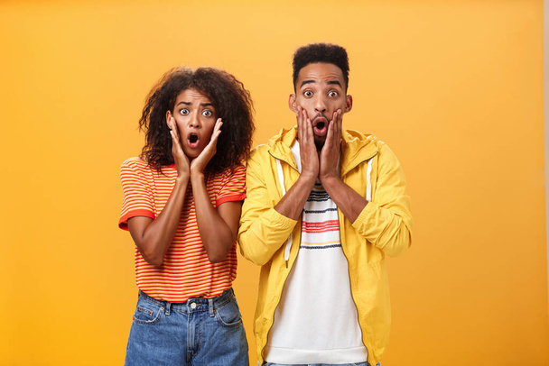 Portrait of shocked and stunned speechless girlfriend dropping jaw from amazement with boyfriend feeling amazed from shook news posing together surprised and astonished over orange wall - Fotoğraf, Görsel