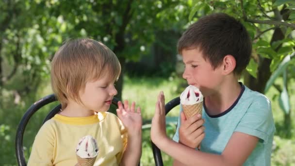 Neşeli küçük çocuklar sıcak bir yaz gününde keyifli ve lezzetli dondurmalar yiyor, çak bir beşlik. - Video, Çekim