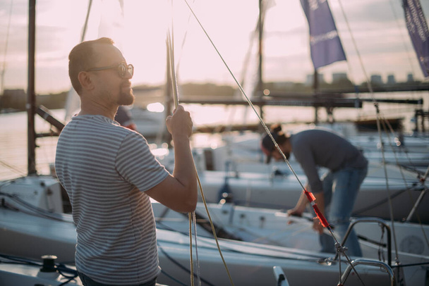 Tourist walks on sailing yachts. Male tourist on vacation on a boat at the sea. Young guy on a moored sport yacht on the lake at sunset. - Valokuva, kuva