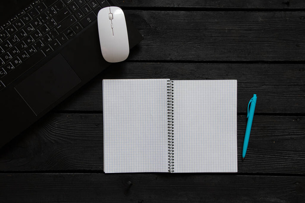 un bloc-notes ouvert et un stylo reposent sur un bureau noir, un ordinateur portable et un ours en peluche, un bureau et un bloc-notes, un endroit pour le texte - Photo, image