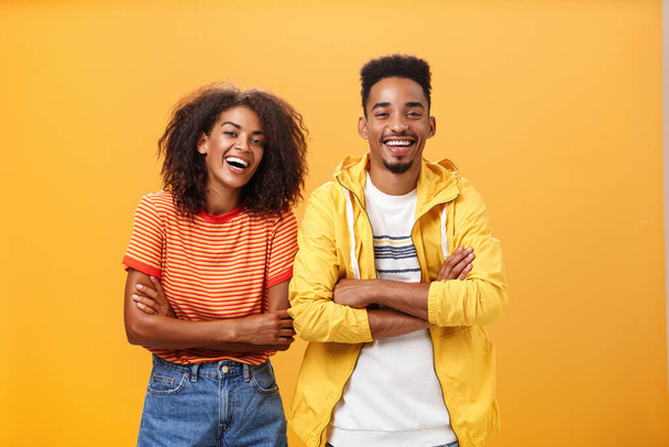 Twee Afro-Amerikaanse mannen en vrouwen die hardop lachen naar grappige films in de bioscoop, gekleed in stijlvolle kleren met gekruiste handen op de borst en geamuseerde uitdrukking - Foto, afbeelding