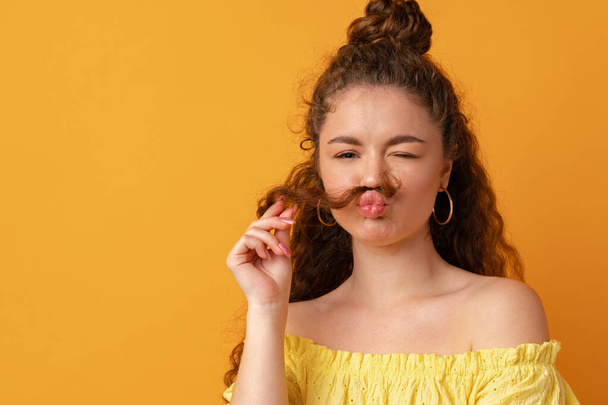 Young woman making moustache with her hair against yellow background - Fotoğraf, Görsel