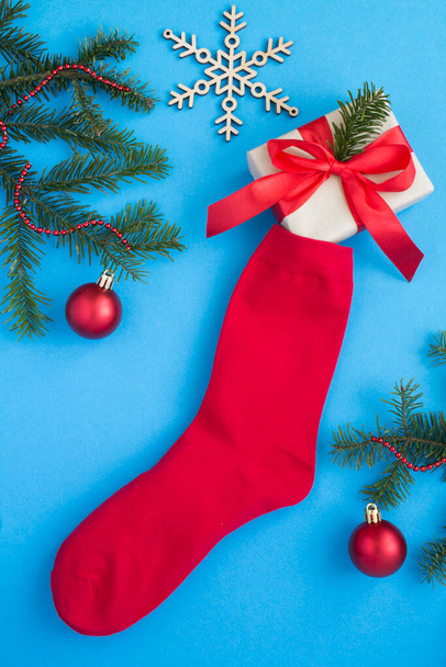 Top view of Christmas red sock with gift box on the blue background. Close-up. - Фото, изображение