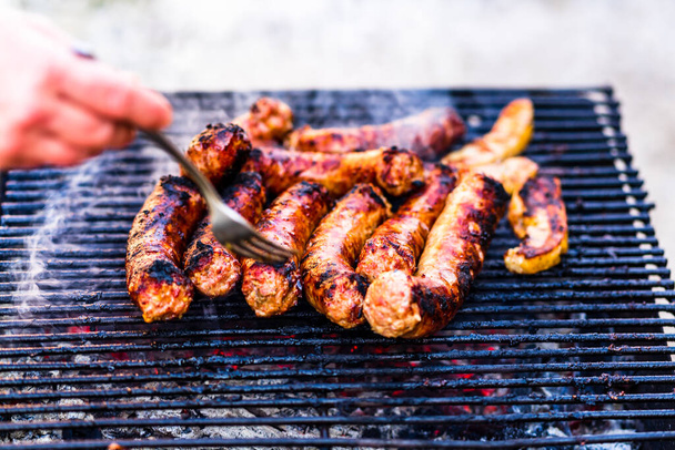 Grilling sausages on barbecue grill. Delicious sausages on charcoal grill - Фото, изображение