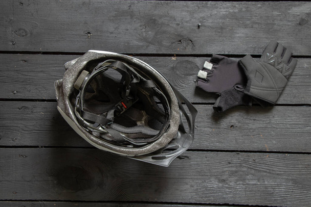 Fahrradhelm und schwarze Handschuhe liegen auf schwarzem Holzhintergrund in Großaufnahme, Schutzhelm zum Radfahren - Foto, Bild