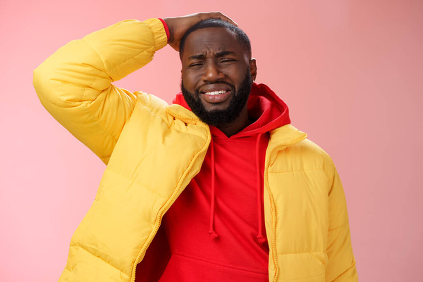Upset gloomy african-american bearded guy in yellow jacket red hoodie hold hands cringing regret face disaster terrible situation expressing sorrow crying sobbing, standing pink background - Photo, Image