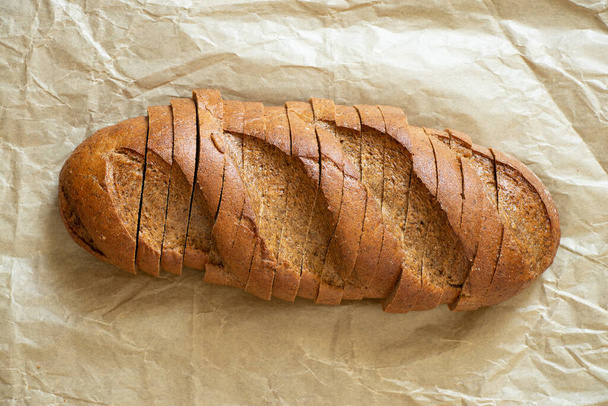 Целая буханка черного нарезанного хлеба лежит на столе из магазина, черный хлеб - Фото, изображение