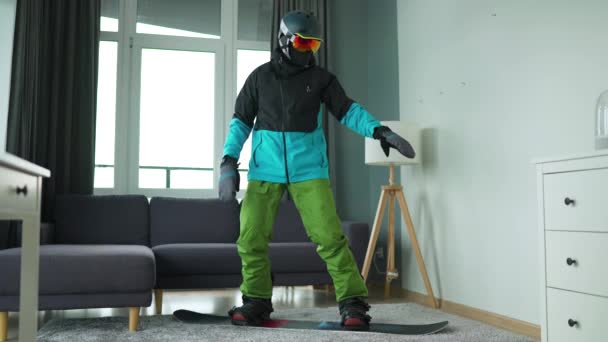 Lustiges Video. Als Snowboarder verkleideter Mann zeigt Snowboarder auf einem Teppich in einem gemütlichen Raum. Warten auf einen schneereichen Winter. Zeitlupe - Filmmaterial, Video