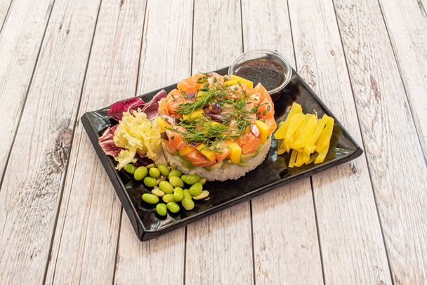 marinated salmon tartare with pieces of red onion, African mango, edamame beans, yellow pepper, white rice and ripe avocado - Foto, afbeelding