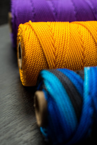 Close-up de alguns rolos coloridos diferentes de linha em uma mesa de madeira preta - Foto, Imagem