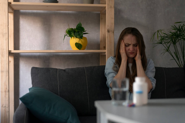 Tabletten auf dem Tisch aus dem Fokus auf den Hintergrund eines Mädchens mit Kopfschmerzen. Frau hält Kopf mit Händen und leidet an Migräne - Foto, Bild