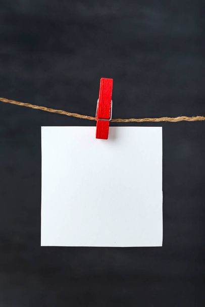 Weiße Blanko-Zettelkarten hängen mit Wäscheklammern am Seil. Schwarzer Hintergrund. Kopierraum, Attrappe. - Foto, Bild