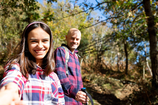 Father and teenage holding hands hiking and looking at camera smiling in the forest. Point Of View Shoot - Foto, Bild