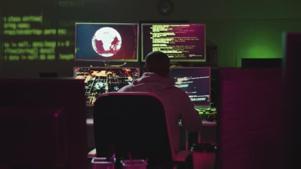Taustakuva kuvaa tunnistamattomasta miehestä, joka istuu pimeässä toimistohuoneessa tietokonenäyttöjen edessä hakkeroimassa tärkeitä tietoja. - Materiaali, video