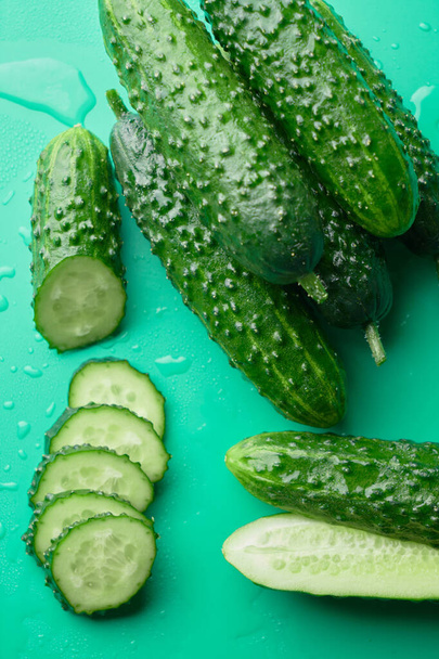 Set of fresh whole and sliced cucumbers on a green background with water drops. Garden cucumber wallpaper backdrop design - Foto, imagen